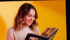 Žena s úsměvem prohlíží rodinné fotoalbum před žlutým pozadím