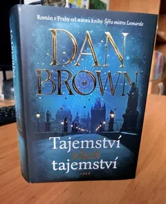 Kniha Dan Brown Tajemství tajemství, obálka se siluetou Prahy na stole